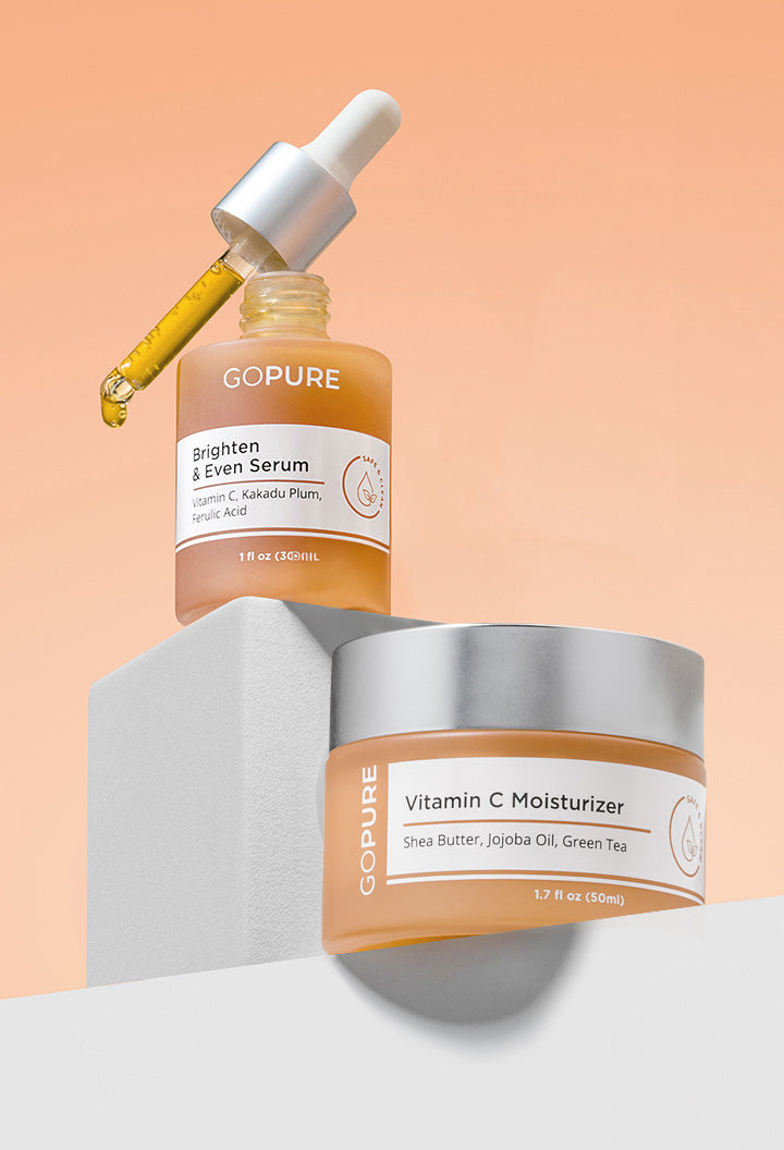 Two GOPURE skincare products on a peach gradient background. The top product is a frosted amber bottle labeled 'Brighten & Even Serum' with a silver dropper releasing golden liquid. The bottom product is a frosted amber jar labeled 'Vitamin C Moisturizer' with a silver lid. Both products feature clean, white labels with minimal text.