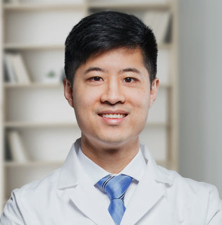 Doctor Chen in white lab coat with blue tie standing in front of a bookshelf.