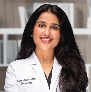 A woman wearing a white lab coat over a black shirt, standing confidently in a professional setting.