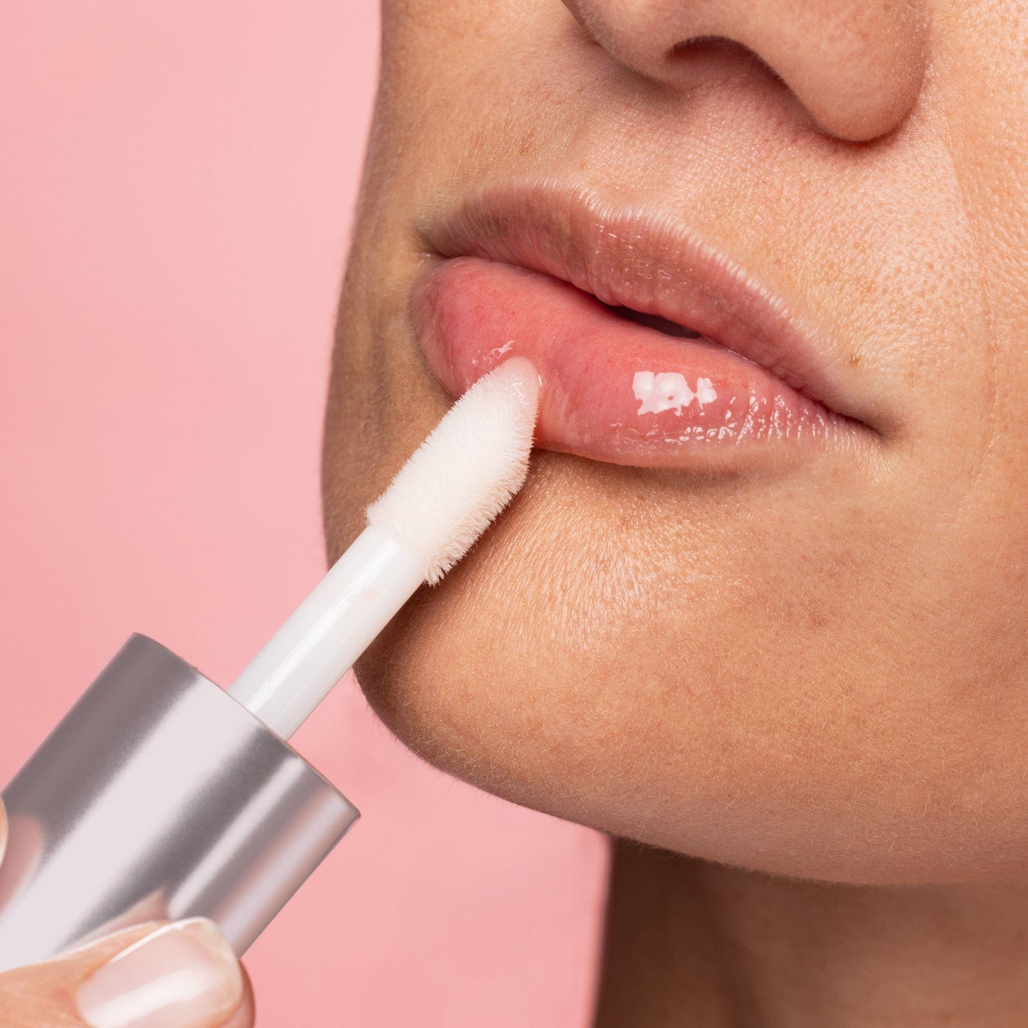 A smear of peach-colored lip gloss on a white background, showcasing its smooth and shiny texture.