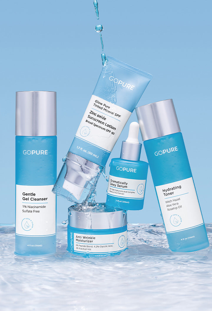 Five GOPURE skincare products displayed against a blue background with water splashes. From left to right: 'Gentle Gel Cleanser' in a tall blue bottle with a silver cap, 'Glow Pure Tinted Mineral SPF' sunscreen lotion in a blue tube, 'Dramatically Dewy Serum' in a blue dropper bottle, 'Anti Wrinkle Moisturizer' in a blue jar with a silver lid, and 'Hydrating Toner' in a blue bottle with a silver cap. The products are arranged dynamically, with water droplets enhancing the fresh, hydrating theme.